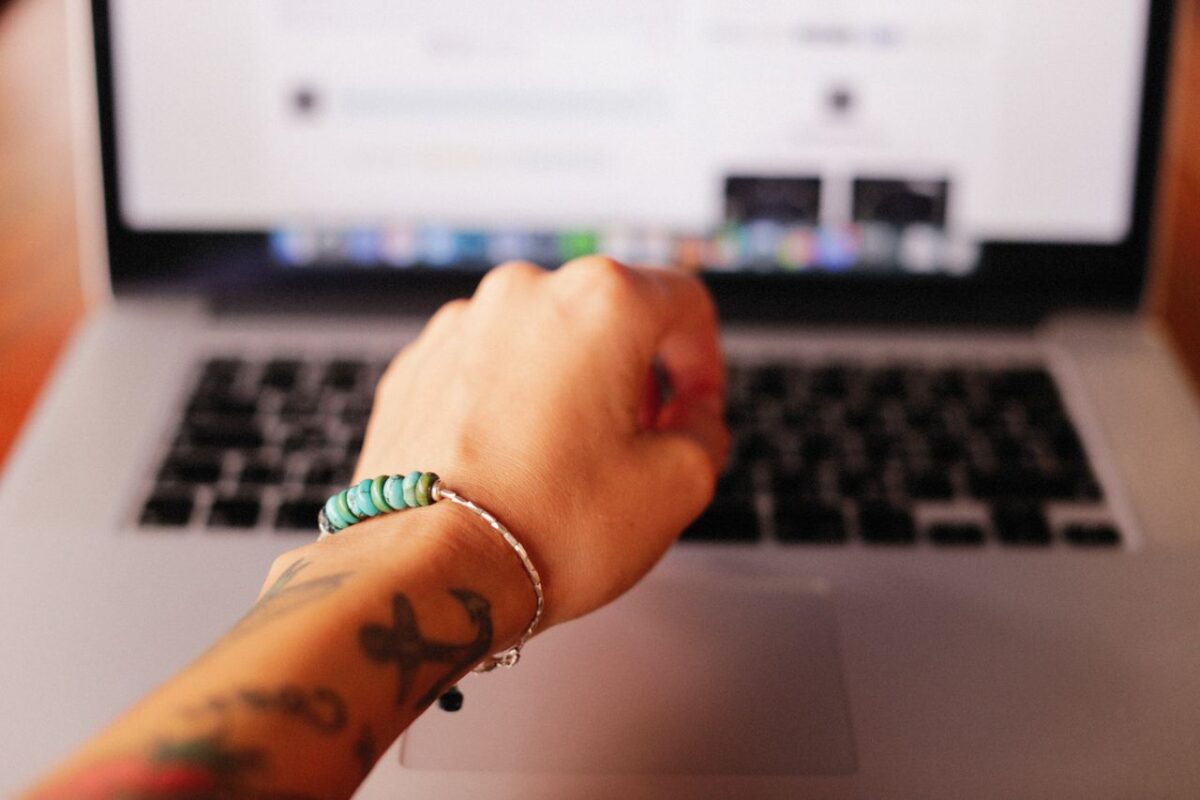 why-choose-us-02 Close-up of a tattooed hand wearing a bracelet typing on a laptop.